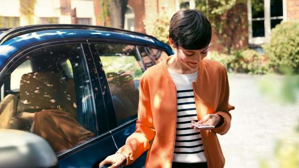 Kobieta patrząca na smartfon w BMW serii 5 Touring G31 Kobieta wysiada z BMW serii 5 Touring G31, modernizacja 2020, zerkając na smartfon