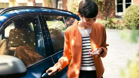 Kobieta patrzy na swój smartfon i otwiera drzwi BMW Kobieta z BMW Teleservices patrzy na swój smartfon i otwiera drzwi BMW