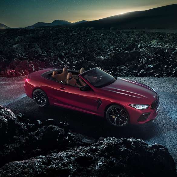 BMW M8 Competition Cabrio, półprofil z boku. BMW M8 Competition Cabrio w metalizowanym kolorze czerwieni Motegi z otwartym dachem, półprofil z boku, stojące w nocy na asfalcie.