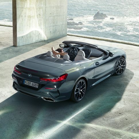 BMW M850i xDrive Cabrio, widok z góry. BMW M850i xDrive Cabrio w metalizowanym kolorze szarego drawitu z otwartym dachem, widok z góry, zaparkowane w metalowej budowli na tle oceanu.