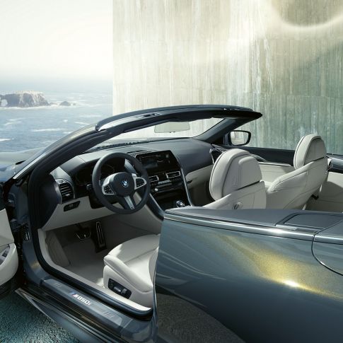 BMW M850i xDrive Cabrio, wnętrze. BMW M850i xDrive Cabrio w metalizowanym kolorze szarego drawitu z otwartym dachem, wnętrze z kierownicą sportową M i tapicerką BMW Individual ze skóry Merino w kolorze kości słoniowej.