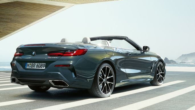 BMW M850i xDrive Cabrio, tylny półprofil. BMW M850i xDrive Cabrio w metalizowanym kolorze szarego drawitu z otwartym dachem, tylny półprofil, zaparkowane z widokiem na ocean.