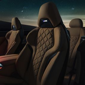 Fotele sportowe M obite skórą Merino. BMW M8 Competition Cabrio z otwartym dachem pod rozgwieżdżonym niebem, wnętrze z fotelami sportowymi M obitymi skórą Merino i czerwonym oświetleniem ambientowym.
