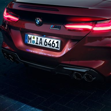 BMW M8 Competition Cabrio, zbliżenie tyłu. BMW M8 Competition Cabrio w metalizowanym kolorze czerwieni Motegi, zbliżenie tyłu z lampami tylnymi LED i znaczkiem M8 Competition.