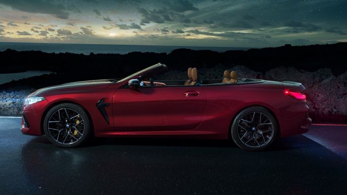 BMW M8 Competition Cabrio, widok z boku. BMW M8 Competition Cabrio w metalizowanym kolorze czerwieni Motegi z otwartym dachem, widok z boku, stojące w nocy pod rozgwieżdżonym niebem.