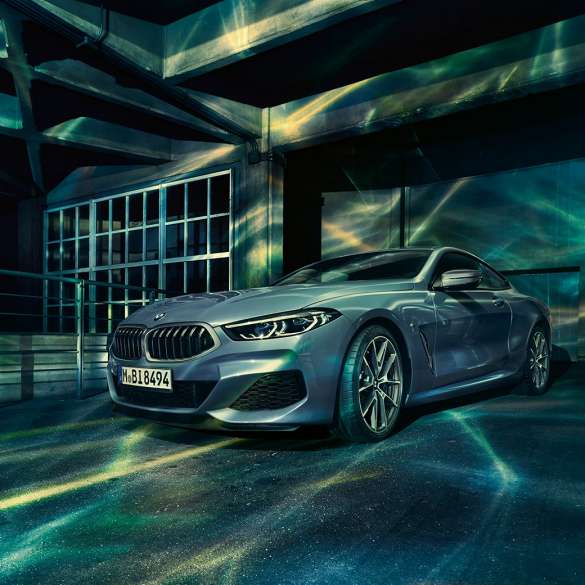 BMW M850i xDrive Coupé, przedni półprofil. BMW M850i xDrive Coupé w metalizowanym kolorze niebieskim Barcelona, przedni półprofil, stojące przed budowlą.