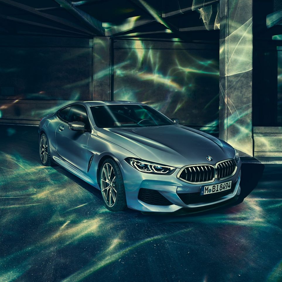 BMW M850i xDrive Coupé, lewy przedni półprofil. BMW M850i xDrive Coupé w metalizowanym kolorze niebieskim Barcelona, lewy przedni półprofil, stojące przed budowlą.