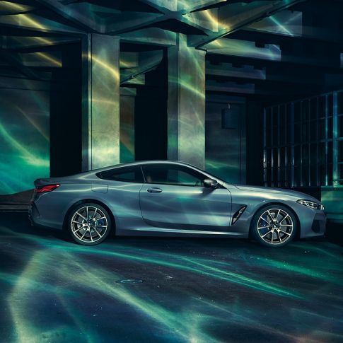 BMW M850i xDrive Coupé, widok z boku. BMW M850i xDrive Coupé w metalizowanym kolorze niebieskim Barcelona, widok z boku, stojące przed budowlą.