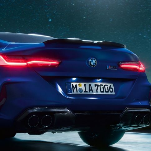 Dyfuzor M w kolorze czarnego karbonu. BMW M8 Competition Coupé w metalizowanym kolorze niebieskim Marina Bay, zbliżenie tyłu w nocy z dyfuzorem M w kolorze czarnego karbonu.