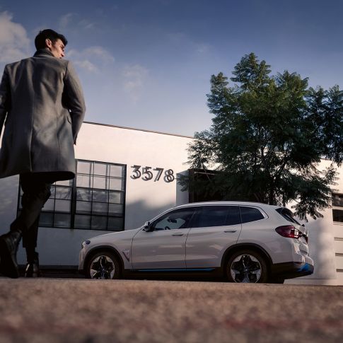 BMW iX3 G08, widok z boku przed budynkiem z mężczyzną BMW iX3 G08 2020, biel mineralna, metalizowany, widok z boku przed budynkiem z mężczyzną