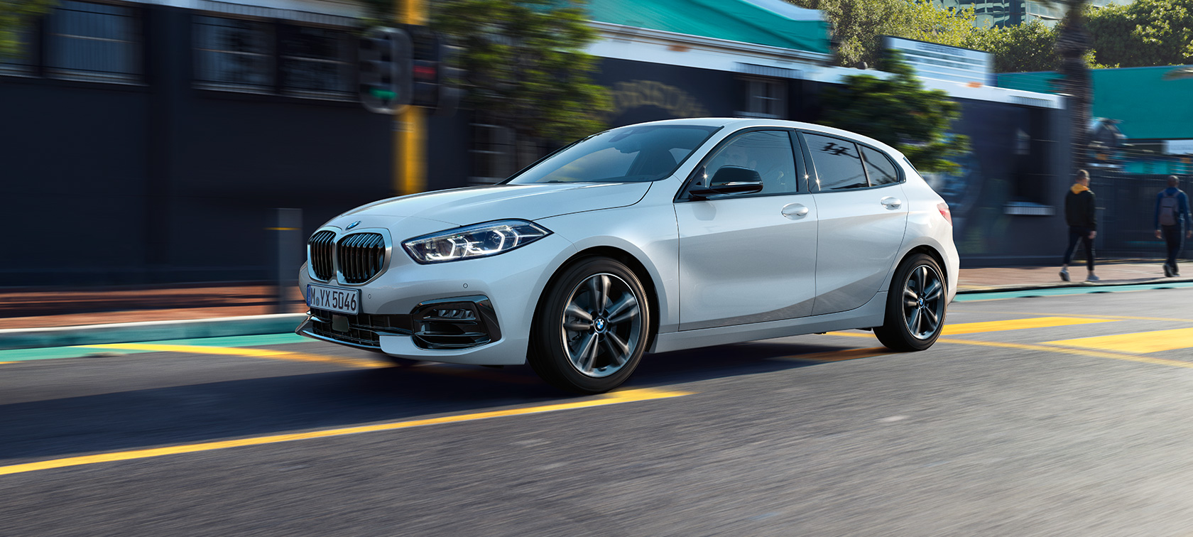 BMW serii 1, model Sport Line, w metalizowanym kolorze bieli mineralnej, półprofil z boku podczas jazdy.