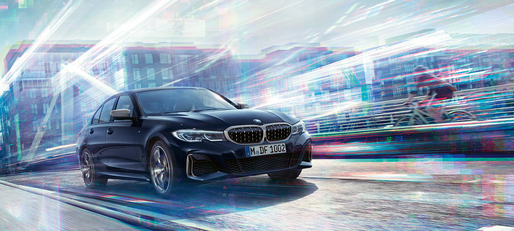 BMW serii 3 Limuzyna, BMWM340i xDrive. Ujęcie trzy-czwarte na bok BMW serii 3 M340i xDrive w ruchu z miejskim tłem.