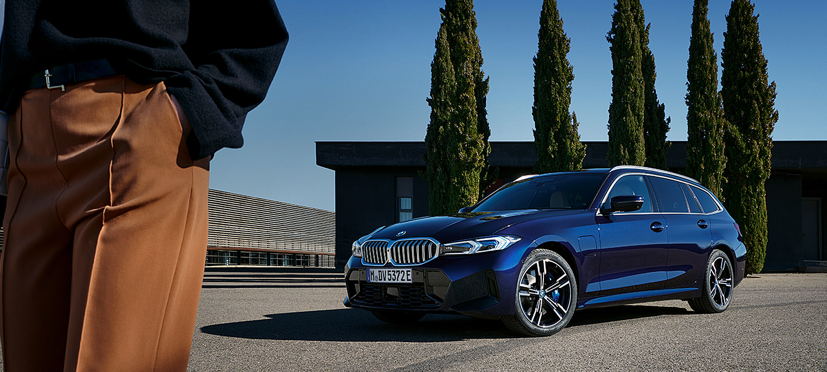 BMW serii 3 Touring LCI G21 niebieski tanzanit II przedni półprofil podczas postoju na tle drzew