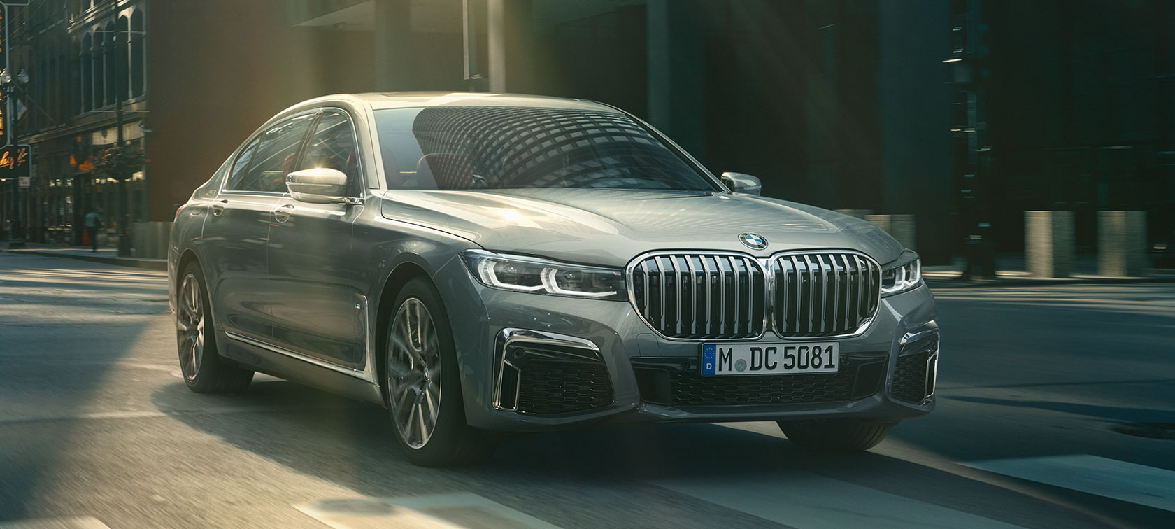 Szare BMW serii 7 Limuzyna podczas jazdy, przedni półprofil Szare BMW serii 7 Limuzyna w przednim półprofilu jedzie przez miasto