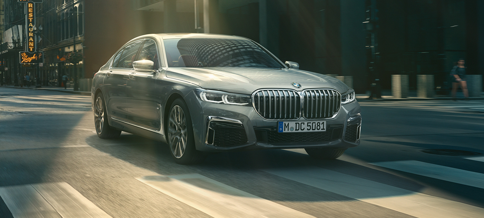Szare BMW serii 7 Limuzyna podczas jazdy, przedni półprofil Szare BMW serii 7 Limuzyna w przednim półprofilu jedzie przez miasto