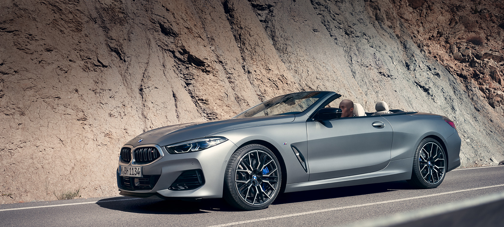 BMW serii 8 Convertible G14 LCI Facelift 2022 z otwartym softtopem jadąc wzdłuż górskiej ściany BMW serii 8 kabriolet G14 LCI Facelift 2022 BMW Individual Frozen Pure Grey metalik widok z boku z otwartym softtopem jazda wzdłuż ściany górskiej