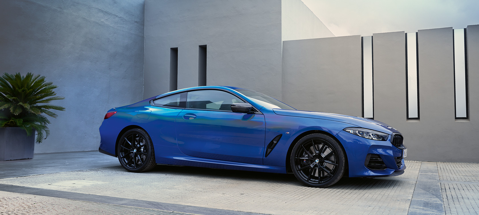 BMW serii 8 Coupé G15 LCI modernizacja 2022 niebieski Portimao M metalizowany widok z boku podczas postoju na tle ściany budynku