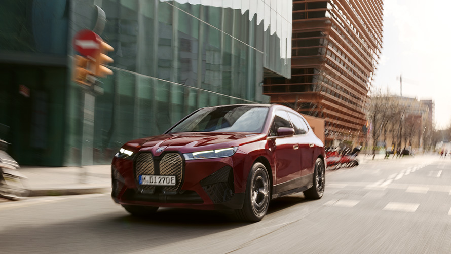 BMW iX i20 elektryczny SUV BMW iX xDrive50 systemy wspomagające kierowcę BMW iX i20 2021 elektryczny SUV BMW iX xDrive50 czerwony awenturyn podczas jazdy w mieście