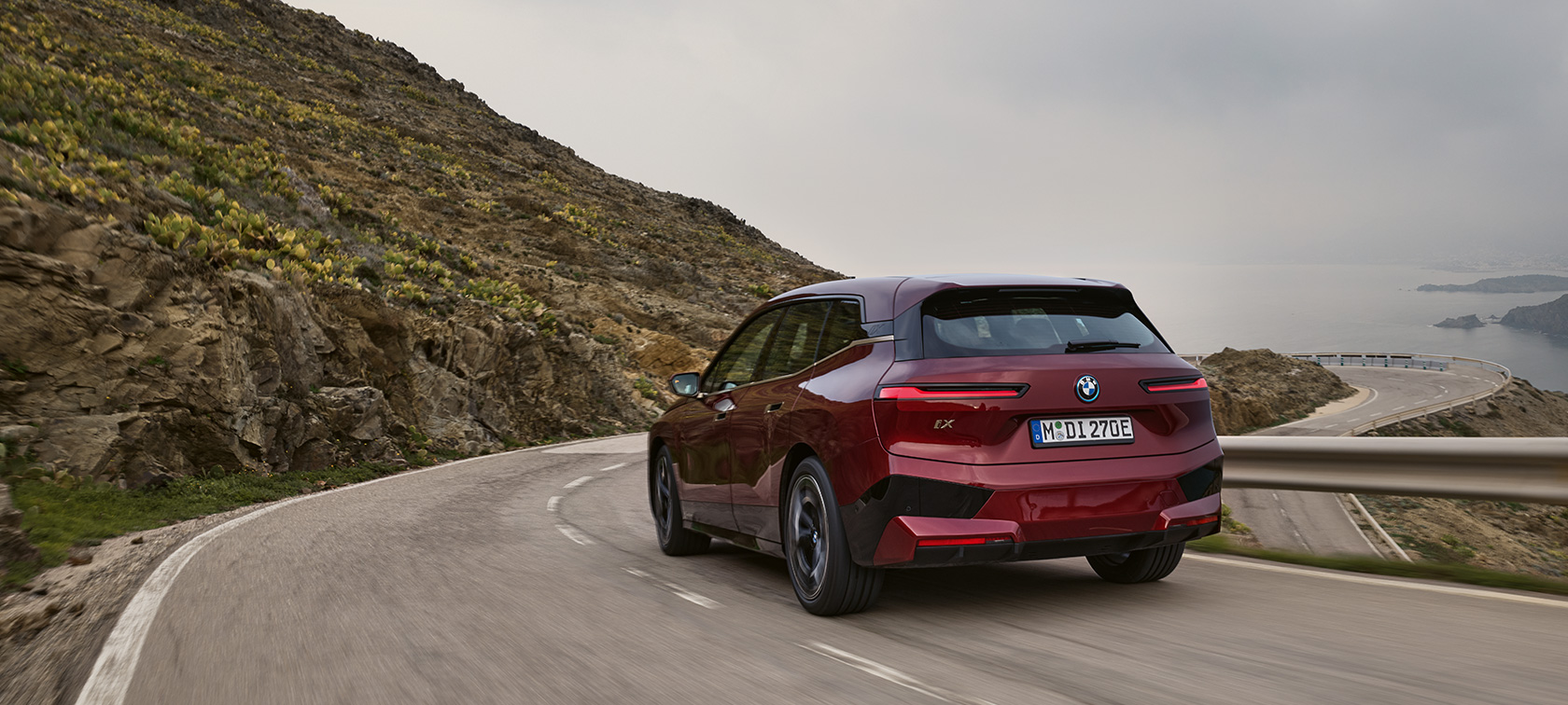 BMW iX i20 2021 elektryczny SUV BMW iX xDrive50 podczas jazdy nadmorską drogą BMW iX i20 2021 elektryczny SUV BMW iX xDrive50 czerwony awenturyn widok z tyłu podczas jazdy nadmorską drogą