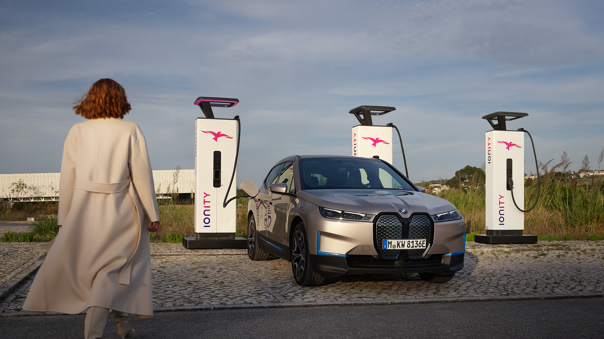 BMW iX, przedni półprofil na stacji ładowania BMW iX, srebrny Kaszmir, i20, przedni półprofil na stacji ładowania