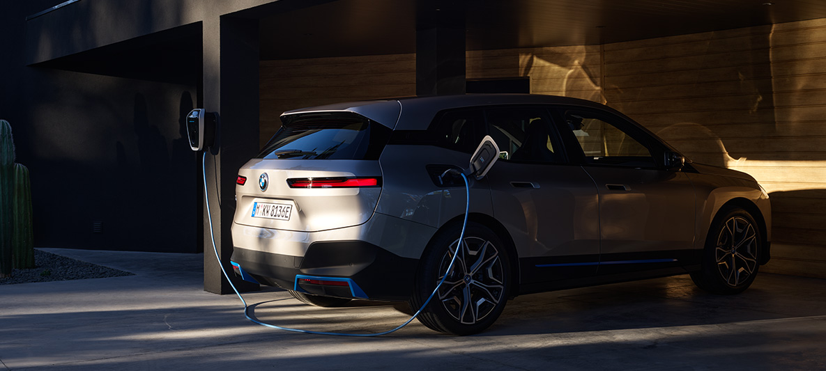 BMW iX, tylny półprofil podczas ładowania z BMW Wallbox BMW iX srebrny Kaszmir i20, tylny półprofil podczas ładowania z BMW Wallbox