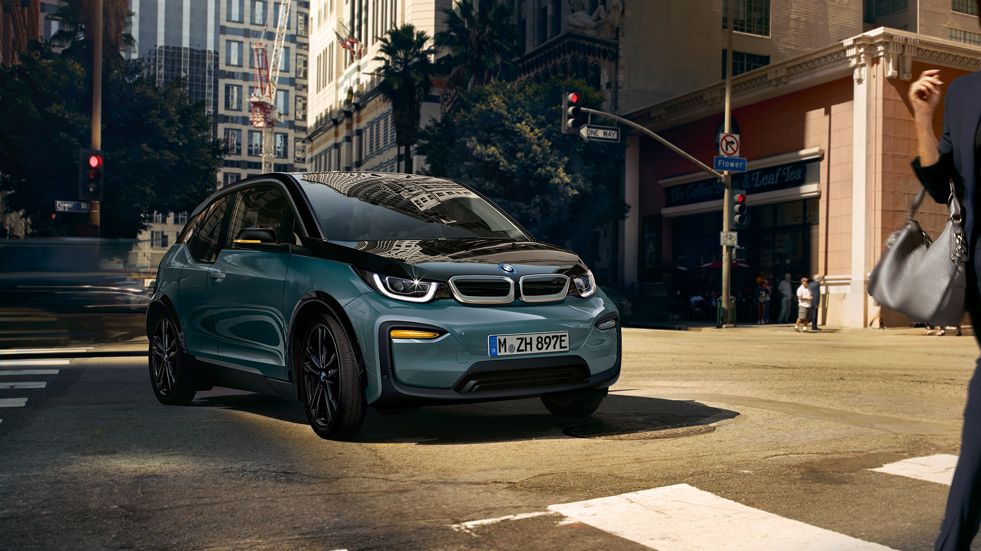 BMW i3 2018, przedni półprofil jadącego samochodu BMW i3 I01 2018, beż Jucaro z akcentami w metalizowanym kolorze mroźnym szarym, przedni półprofil jadącego samochodu na tle miasta