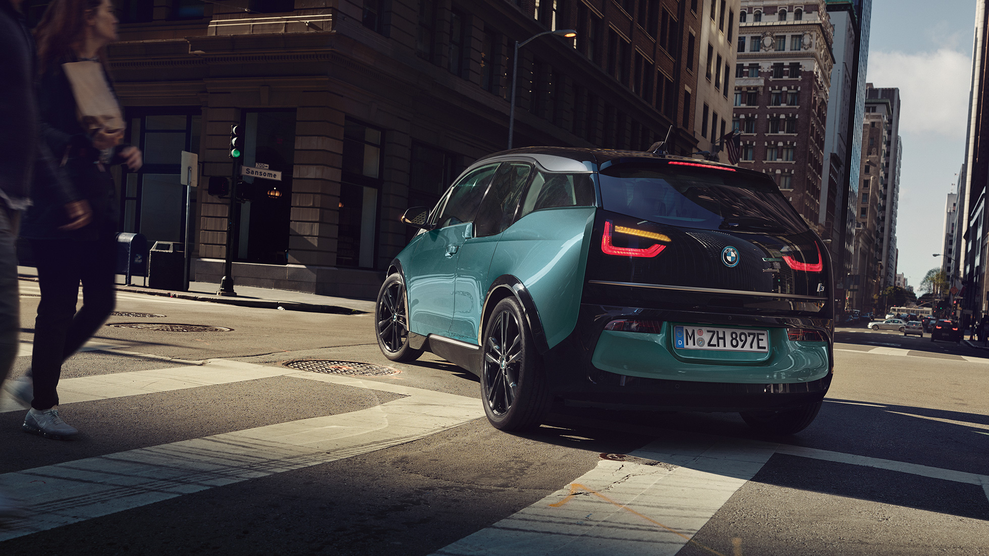 BMW i3 2018, tylny półprofil jadącego samochodu BMW i3 I01 2018, beż Jucaro z akcentami w metalizowanym kolorze mroźnym szarym, tylny półprofil jadącego samochodu na tle miasta