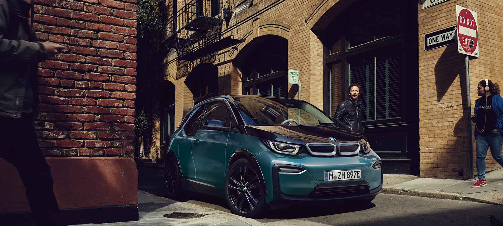BMW i3 2018, przedni półprofil zaparkowanego samochodu BMW i3 I01 2018, beż Jucaro z akcentami w metalizowanym kolorze mroźnym szarym, przedni półprofil parkującego samochodu na tle miasta