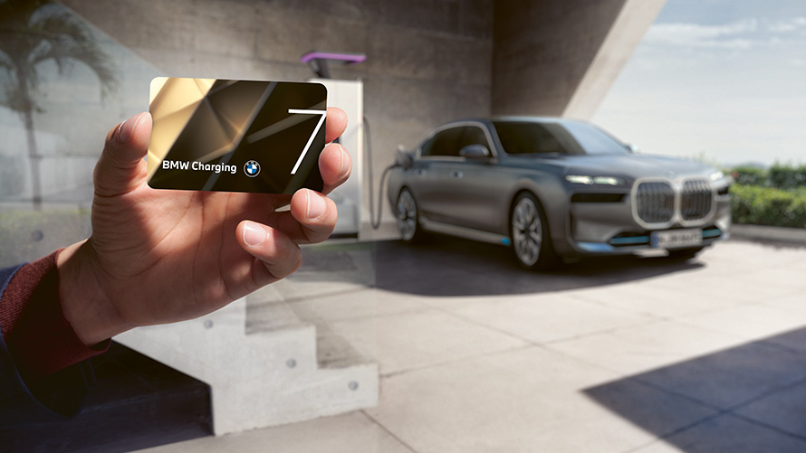 Pakiet do ładowania BMW Charging BMW i7 Limuzyna G70 BMW i7 Limuzyna G70 pakiet do ładowania karta BMW Charging w ręku z BMW i7 w tle