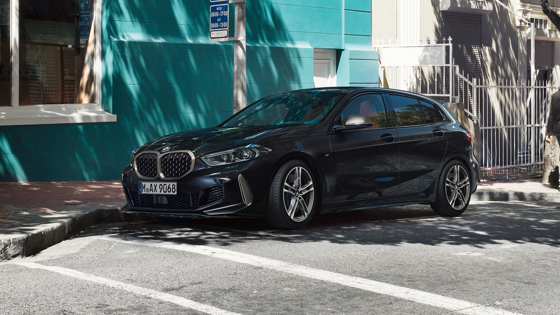 BMW M135i xDrive, półprofil z boku. BMW M135i xDrive w metalizowanym kolorze szafirowoczarnym, półprofil z boku, samochód zaparkowany.