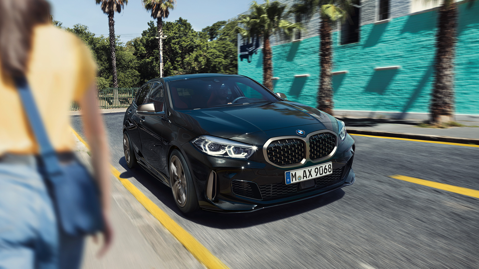 BMW M135i xDrive, przedni półprofil. BMW M135i xDrive w metalizowanym kolorze szafirowoczarnym, przedni półprofil podczas jazdy, z kobietą na pierwszym planie.