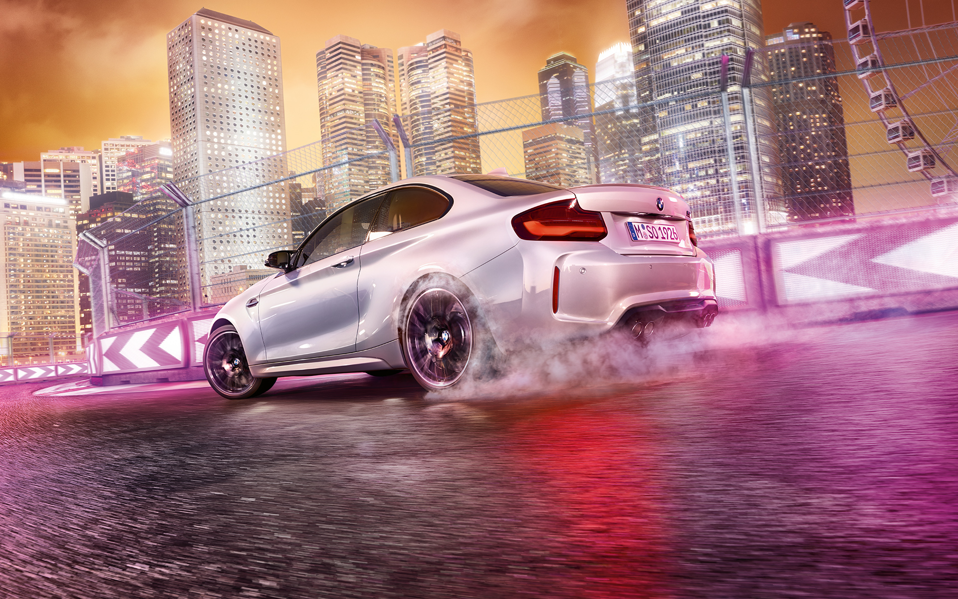 BMW M2 Competiotion w ruchu przyspieszenia. Białe BMW M2 Competition driftująca na torze wyścigowym przed nocną panoramą.