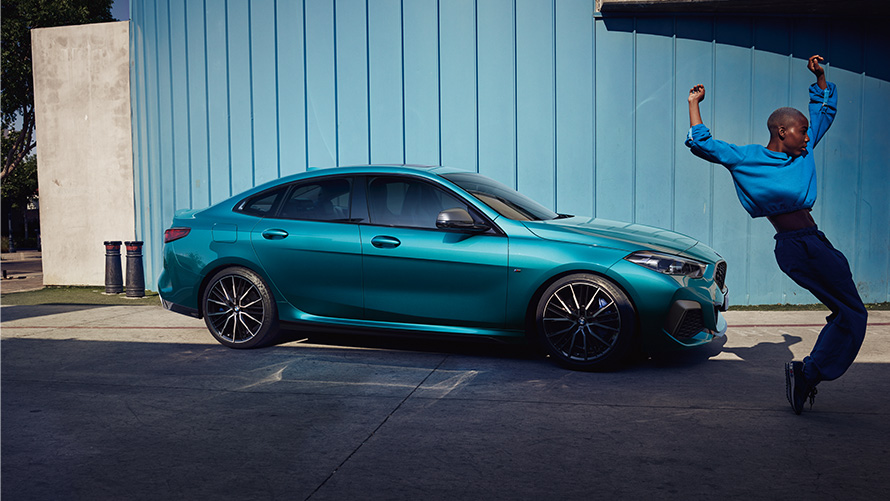 BMW M235i xDrive Gran Coupé F44 widok z boku z kobietą na pierwszym planie BMW M235i xDrive Gran Coupé F44 niebieski Snapper Rocks metalizowany widok z boku z kobietą na pierwszym planie