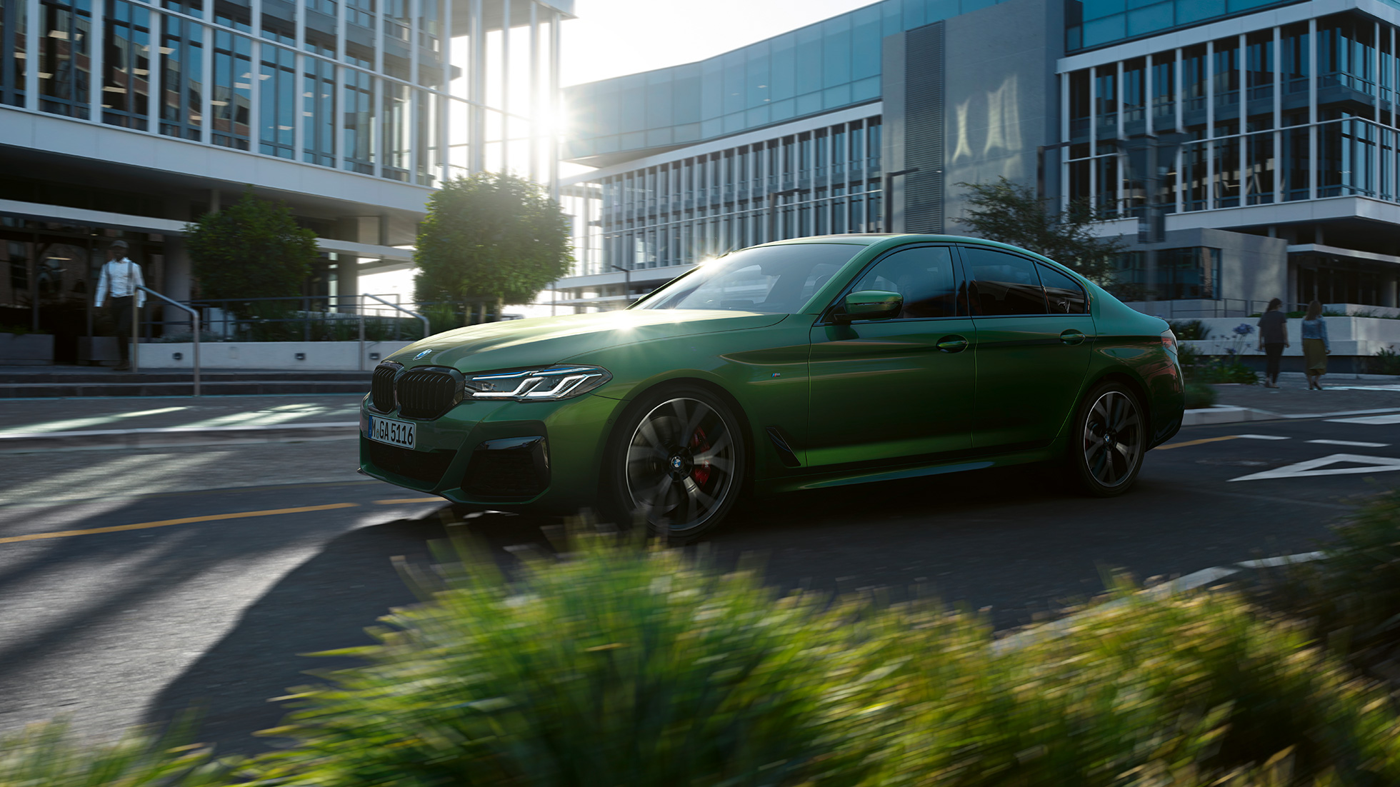 BMW M550i xDrive Limuzyna G30 LCI Facelift 2020, widok z boku podczas jazdy BMW M550i xDrive Limuzyna G30 LCI Facelift 2020 BMW Individual, Verde Ermes metalizowany widok z boku podczas jazdy w mieście