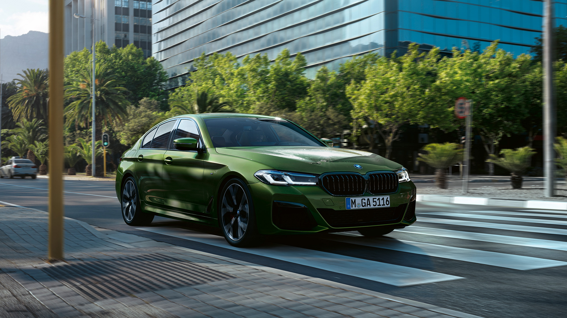 BMW M550i xDrive Limuzyna G30 LCI Facelift 2020, przedni półprofil podczas jazdy BMW M550i xDrive Limuzyna G30 LCI Facelift 2020 BMW Individual, Verde Ermes metalizowany przedni półprofil podczas jazdy w mieście