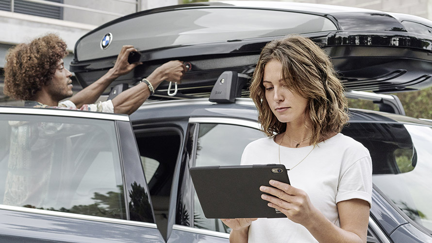 Kobieta z tabletem, mężczyzna montujący bagażnik dachowy BMW BMW Financial Services, leasing BMW, Kobieta z tabletem, mężczyzna montujący bagażnik dachowy BMW