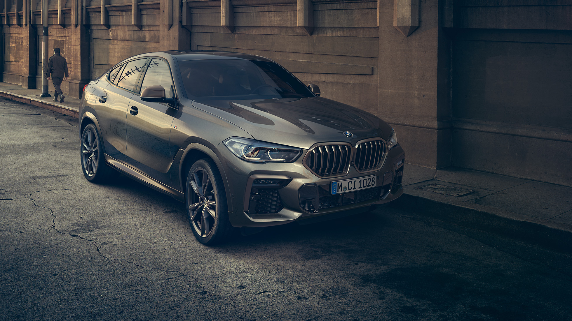 BMW X6 M50i stojący w miejscu. BMW X6 M50i, ujęcie w półprofilu od przodu pojazdu stojącego na tle scenerii miejskiej.