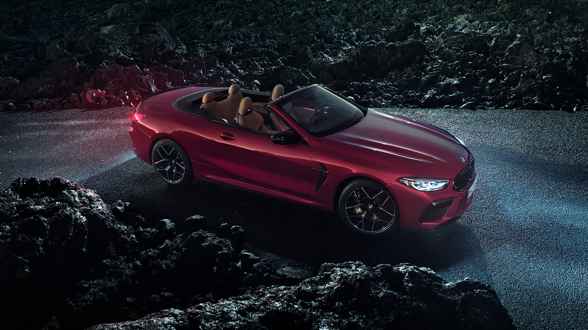 BMW M8 Competition Cabrio, półprofil z boku. BMW M8 Competition Cabrio w metalizowanym kolorze czerwieni Motegi z otwartym dachem, półprofil z boku, stojące w nocy na asfalcie.