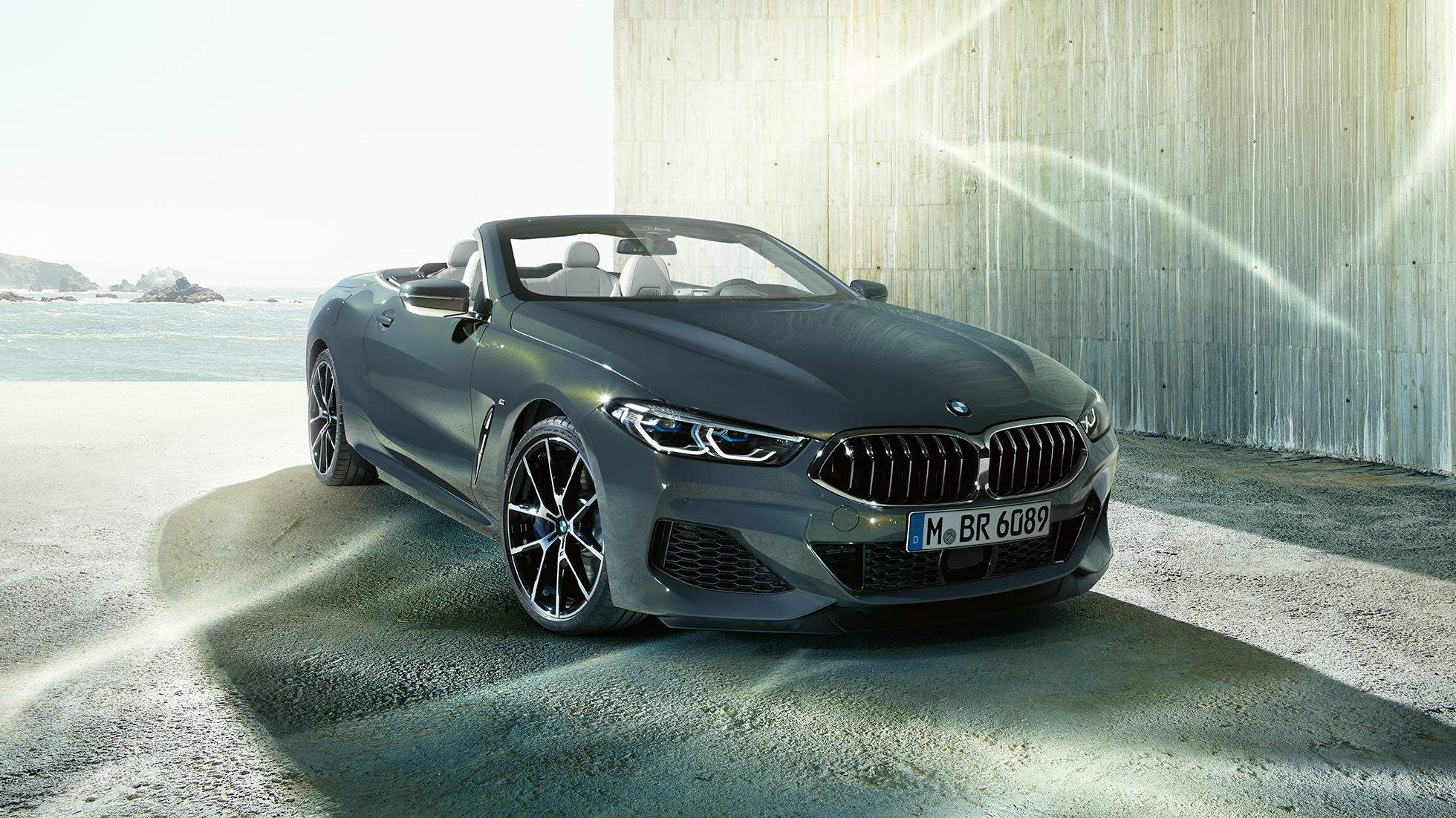 BMW M850i xDrive Cabrio, przedni półprofil. BMW M850i xDrive Cabrio w metalizowanym kolorze szarego drawitu z otwartym dachem, przedni półprofil, stojące przed wybrzeżem.