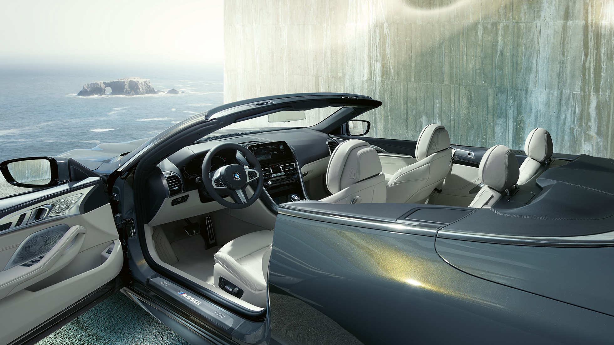 BMW M850i xDrive Cabrio, wnętrze. BMW M850i xDrive Cabrio w metalizowanym kolorze szarego drawitu z otwartym dachem, wnętrze z kierownicą sportową M i tapicerką BMW Individual ze skóry Merino w kolorze kości słoniowej.