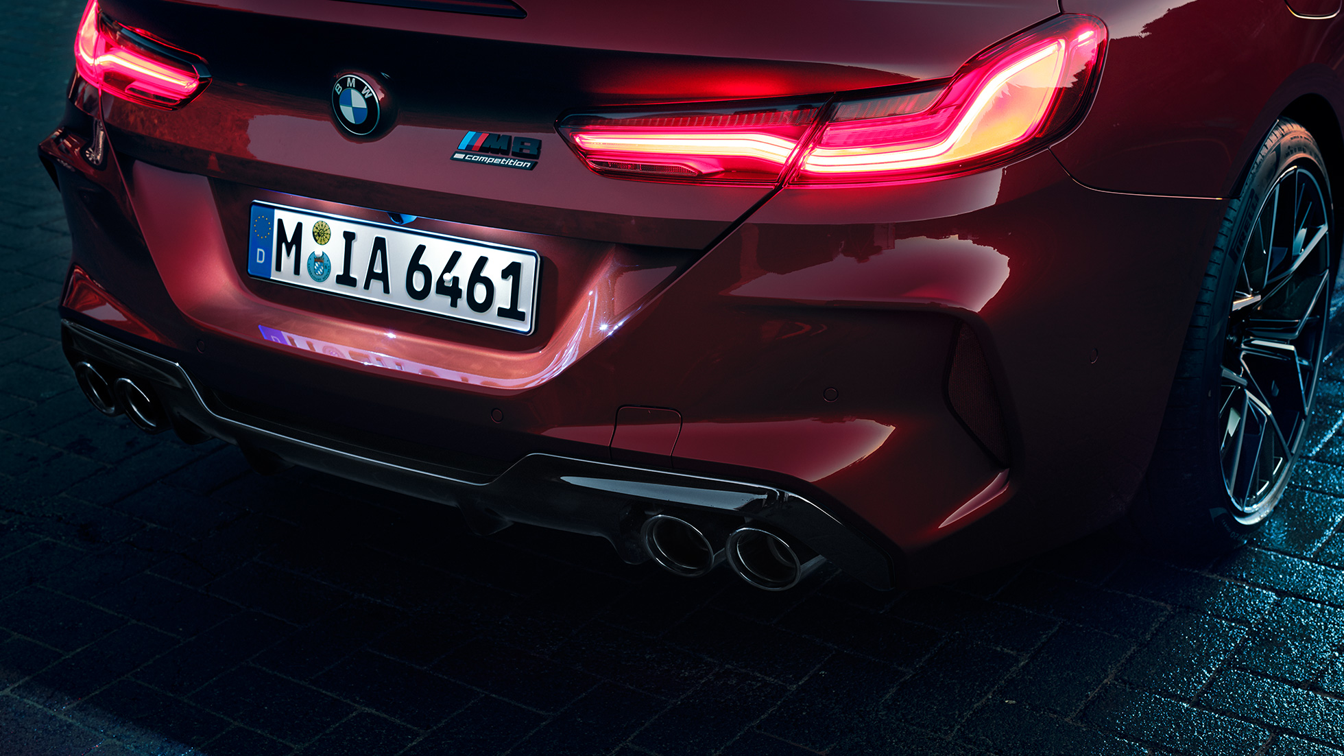 BMW M8 Competition Cabrio, zbliżenie tyłu. BMW M8 Competition Cabrio w metalizowanym kolorze czerwieni Motegi, zbliżenie tyłu z lampami tylnymi LED i znaczkiem M8 Competition.