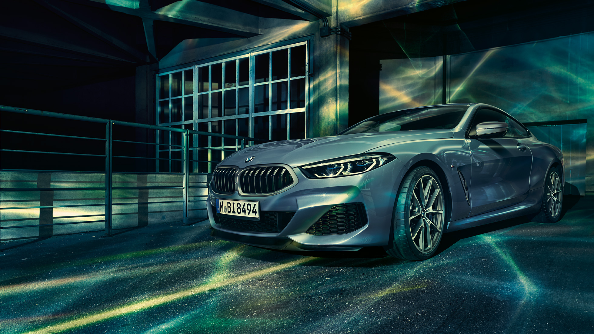 BMW M850i xDrive Coupé, przedni półprofil. BMW M850i xDrive Coupé w metalizowanym kolorze niebieskim Barcelona, przedni półprofil, stojące przed budowlą.