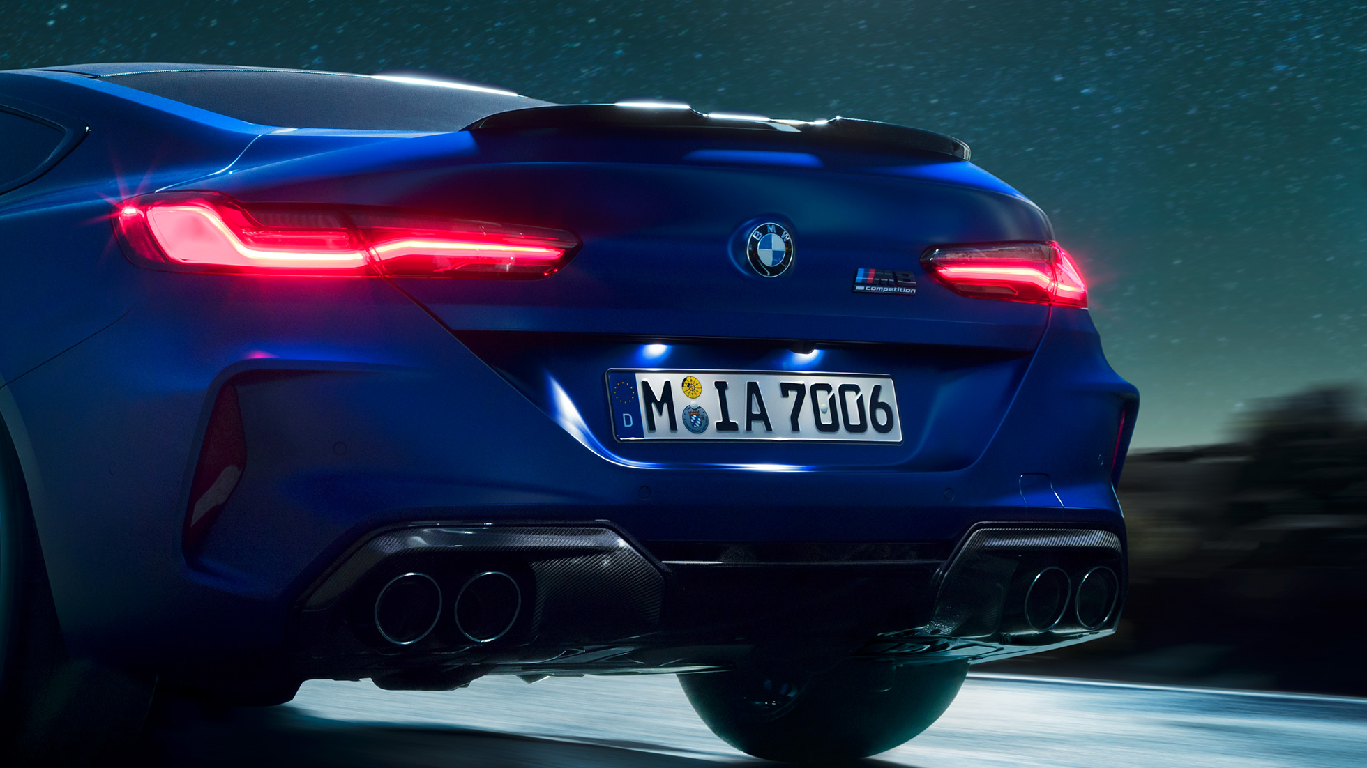 Dyfuzor M w kolorze czarnego karbonu. BMW M8 Competition Coupé w metalizowanym kolorze niebieskim Marina Bay, zbliżenie tyłu w nocy z dyfuzorem M w kolorze czarnego karbonu.