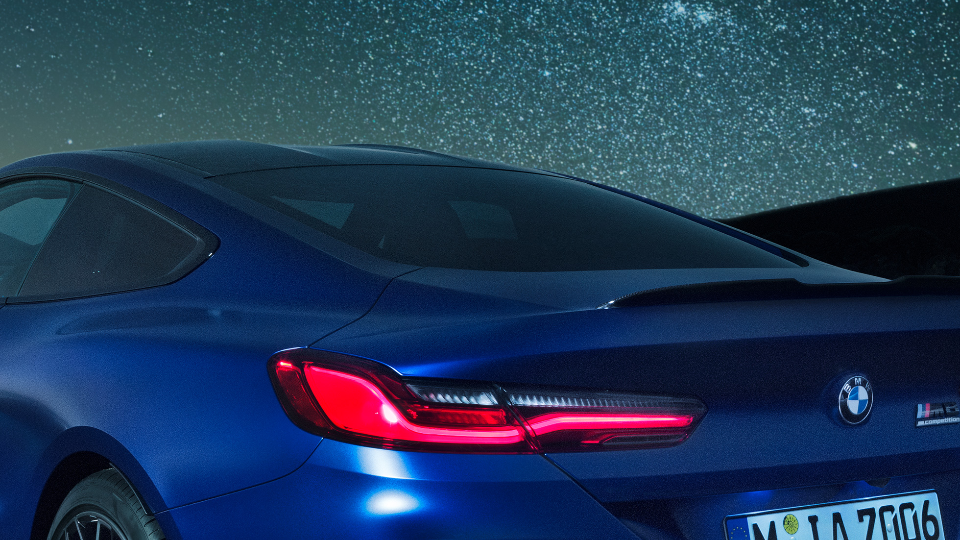Spojler tylny M BMW M8 Competition Coupé w metalizowanym kolorze niebieskim Marina Bay, nocne ujęcie partii barkowej karoserii ze spojlerem tylnym M z karbonu.