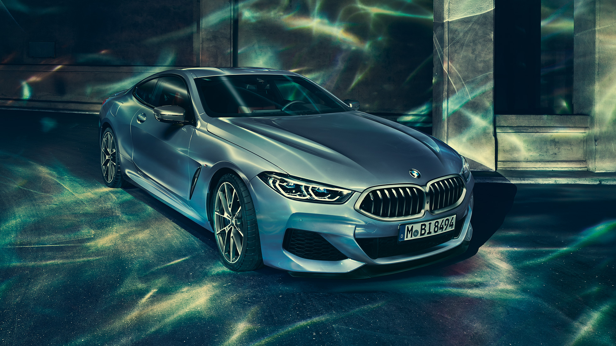 BMW M850i xDrive Coupé, lewy przedni półprofil. BMW M850i xDrive Coupé w metalizowanym kolorze niebieskim Barcelona, lewy przedni półprofil, stojące przed budowlą.
