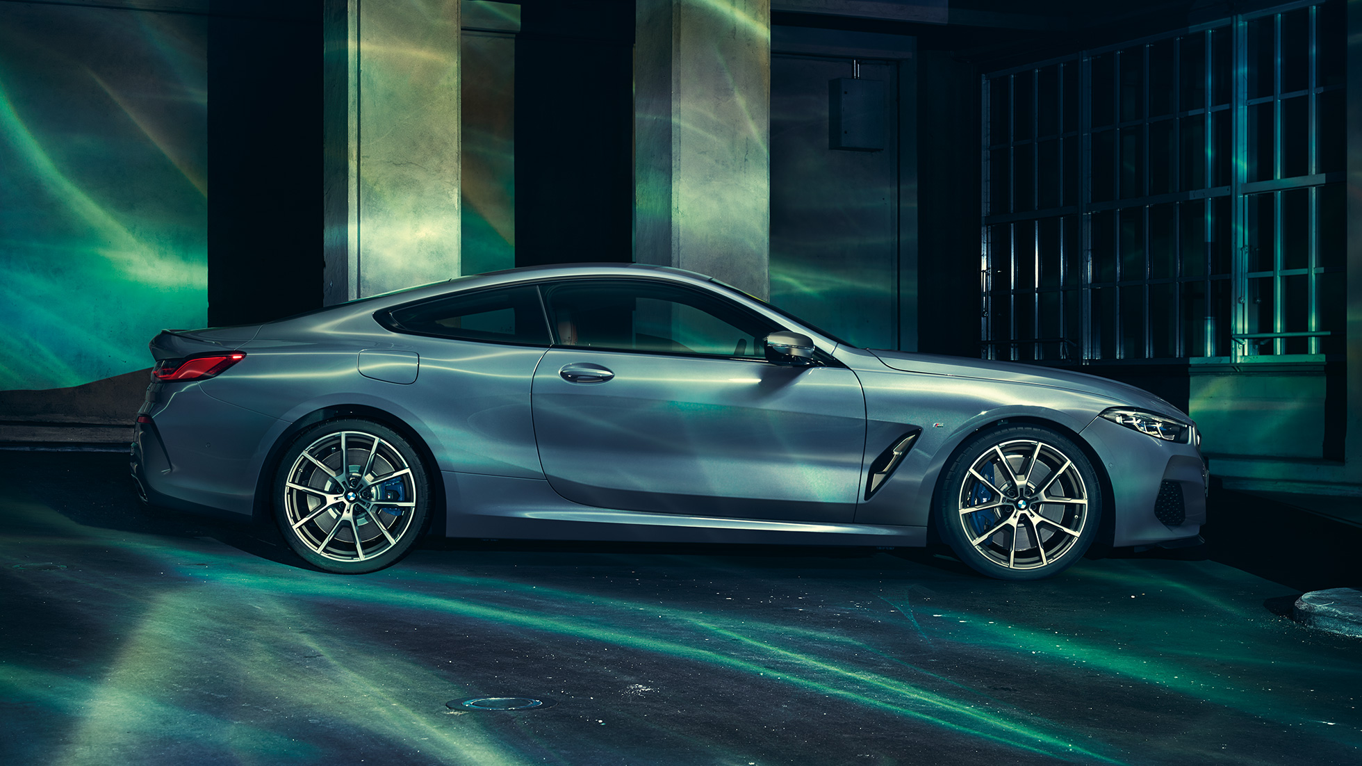 BMW M850i xDrive Coupé, widok z boku. BMW M850i xDrive Coupé w metalizowanym kolorze niebieskim Barcelona, widok z boku, stojące przed budowlą.