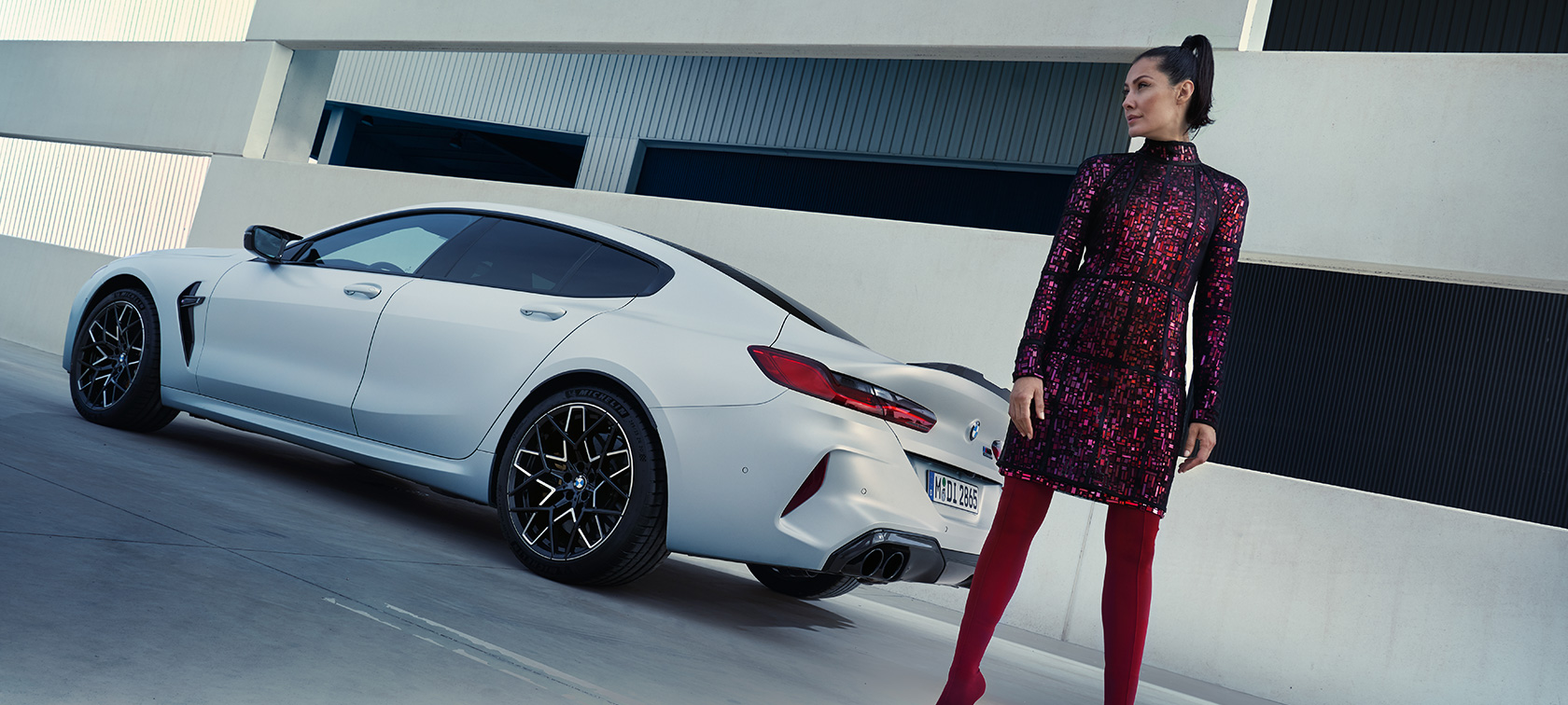 Tylny półprofil BMW M8 Competition Gran Coupé F93 LCI 2022 BMW M8 Competition Gran Coupé F93 LCI modernizacja 2022 mroźna brylantowa biel BMW Individual metalizowany tylny półprofil z modelką obok pojazdu