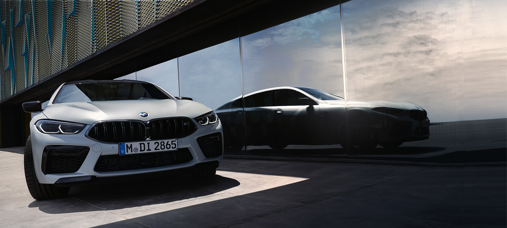 Widok z przodu BMW M8 Competition Gran Coupé F93 LCI modernizacja 2022 BMW M8 Competition Gran Coupé F93 LCI modernizacja 2022 mroźna brylantowa biel BMW Individual metalizowany widok z przodu z odbiciem sylwetki w szybie fasady