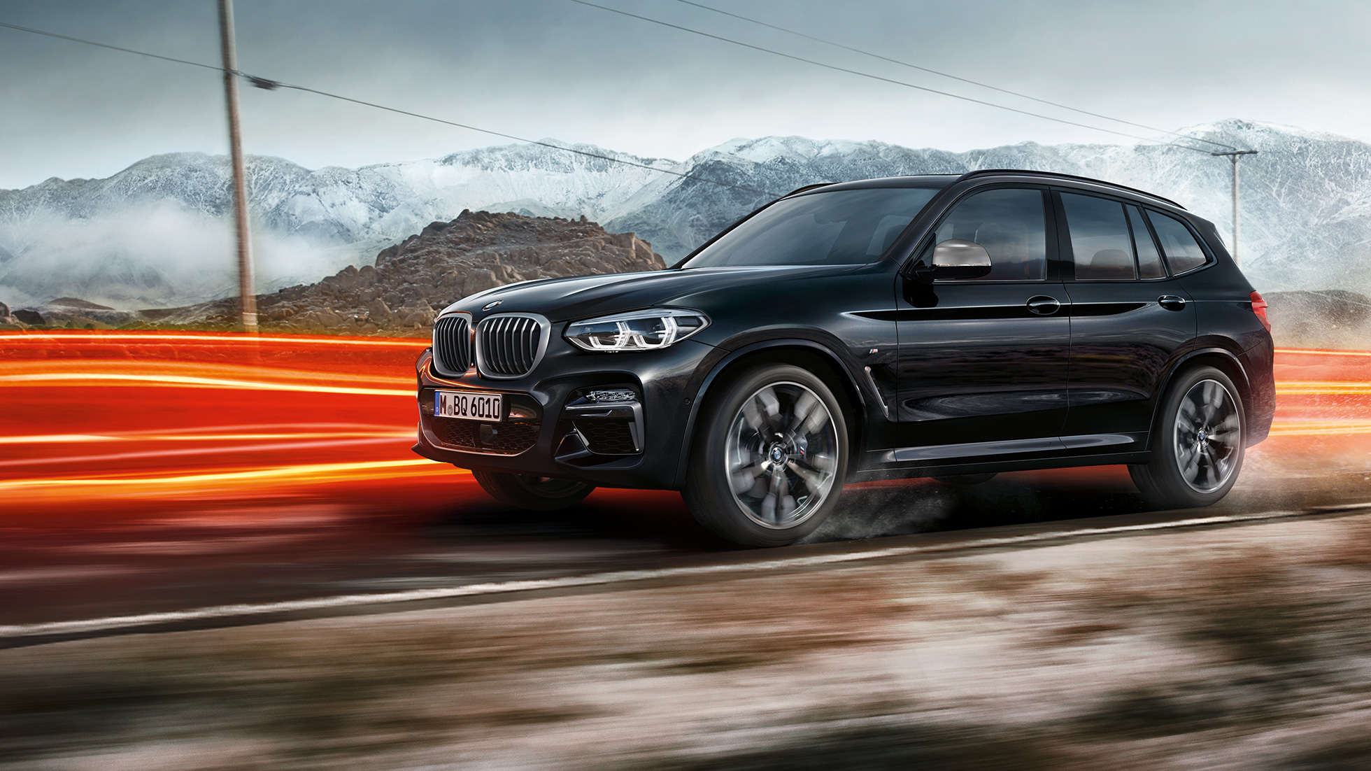 BMW X3 M40i oraz BMW X3 M40d, widok z boku. BMW X3 M40i oraz BMW X3 M40d, szafirowoczarny metalizowany, podczas jazdy, wygląd zewnętrzny, widok boczny na tle gór z pasami świetlnymi.
