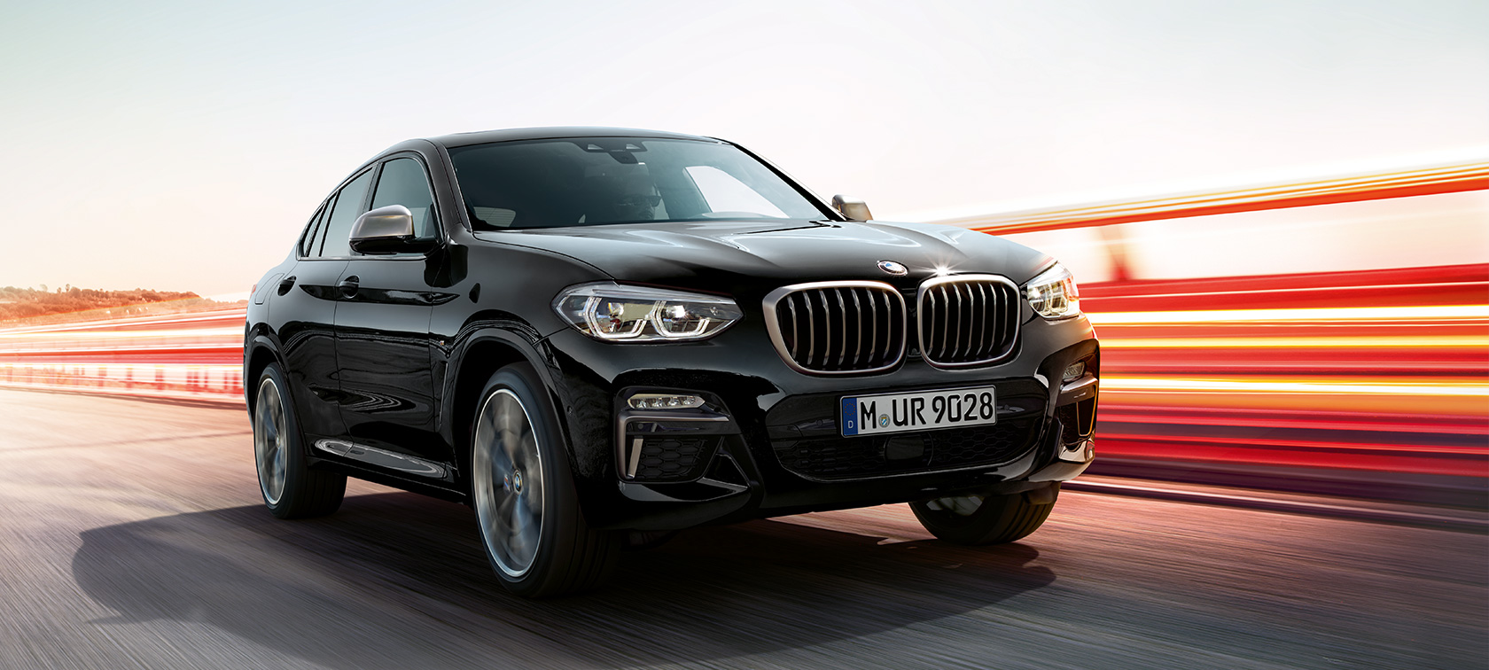 BMW X4 M40i oraz BMW X4 M40d, lewy przedni półprofil. BMW X4 M40i oraz BMW X4 M40d, szafirowa czerń metalizowany, podczas jazdy, widok, wygląd zewnętrzny, półprofil z lewej z pasami świetlnymi.